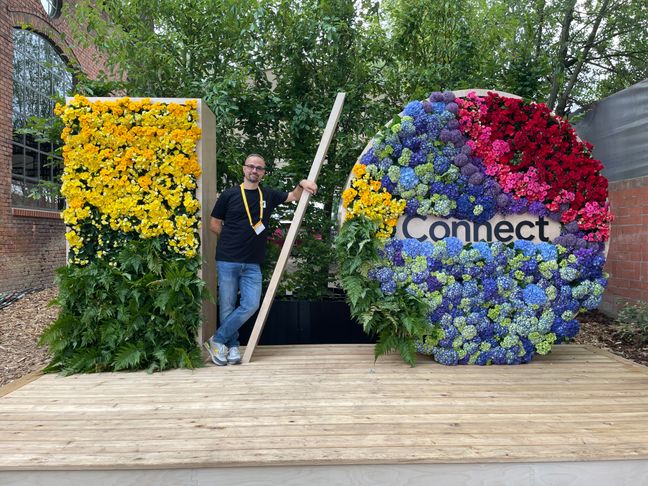 Andrea Verlicchi leaning on the slash between the I and the O of the Google I/O Connect logo covered in flowers